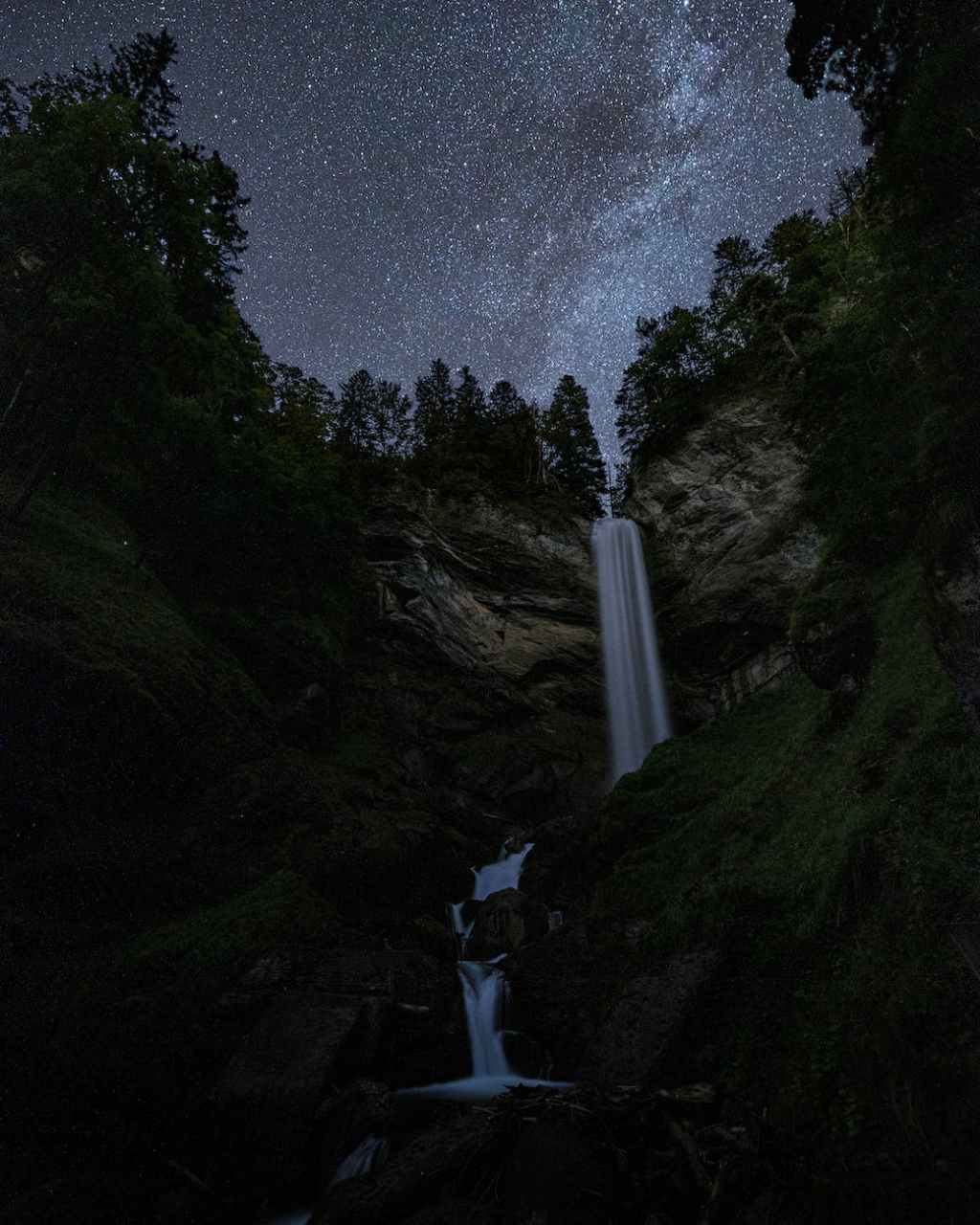 low angle shot of waterfall on mountain under the starry night sky